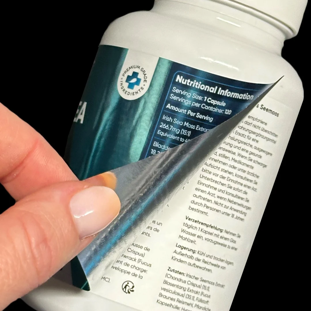 Close-up of a premium Irish Sea Moss supplement bottle — teal label peeled back to reveal the hidden nutritional panel, multilingual ingredient list and dosage instructions on the inner ply